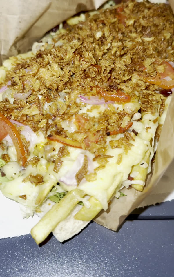 Américain gratiné garni d'oignons frits, de tomate, de fromage fondu et de frites, dans son papier kraft