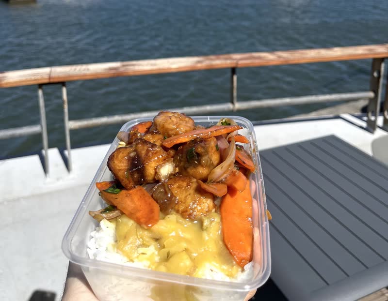 Barquette de poulet sauce caramel, carottes et riz, devant l'eau du port